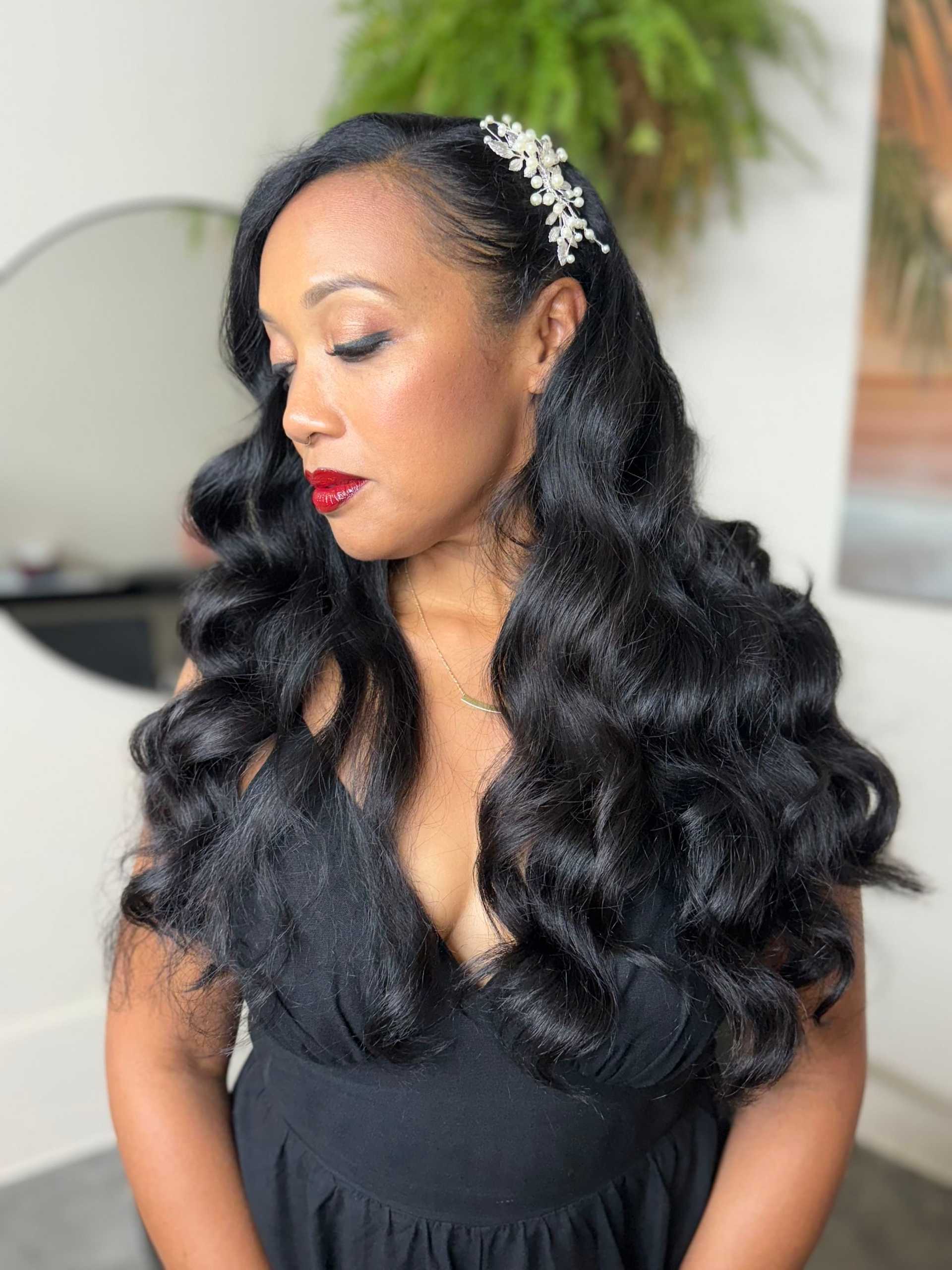Woman with long, wavy hair and floral hairpiece, wearing a black dress, looking down.