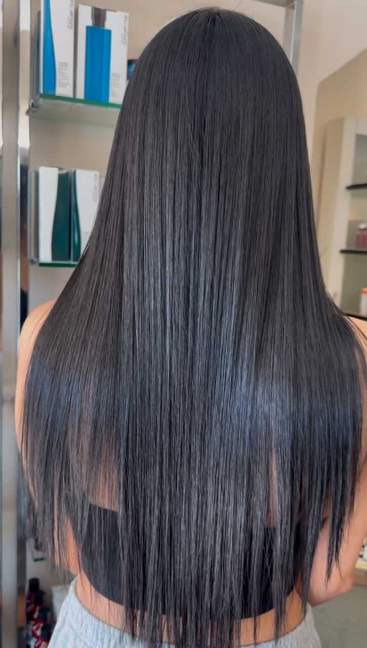 Smooth, straight black hair in a salon setting, with shelves of hair products behind.