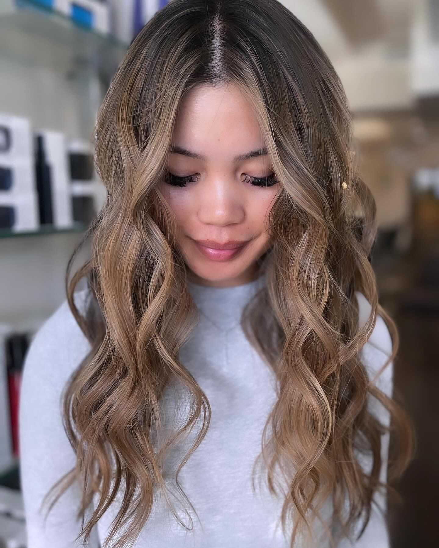 Long wavy-haired person in a light gray top, standing indoors.