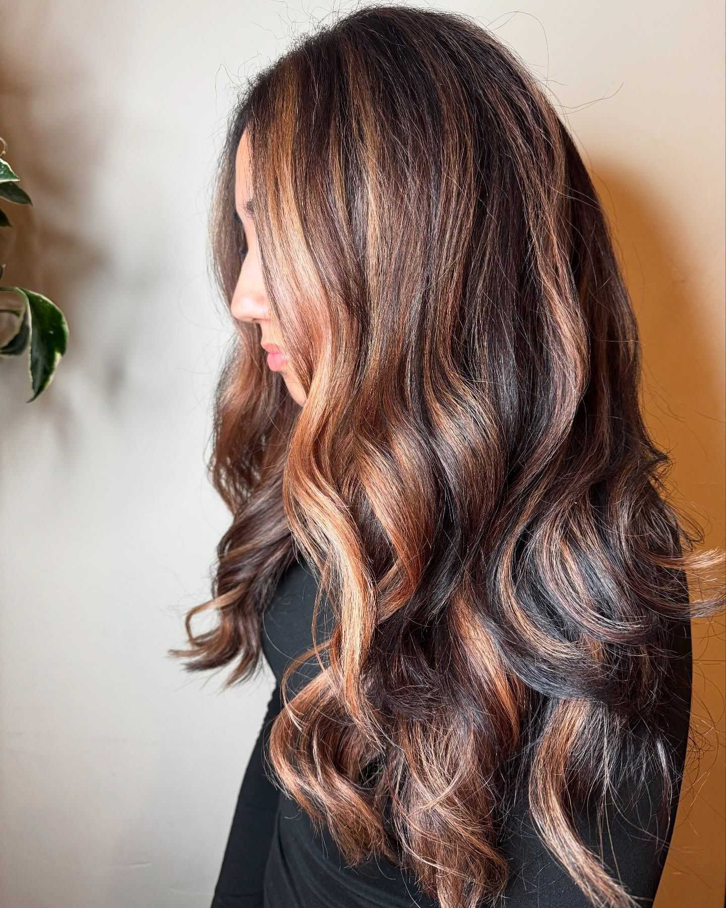 Side profile of a woman with long, wavy hair featuring caramel highlights.
