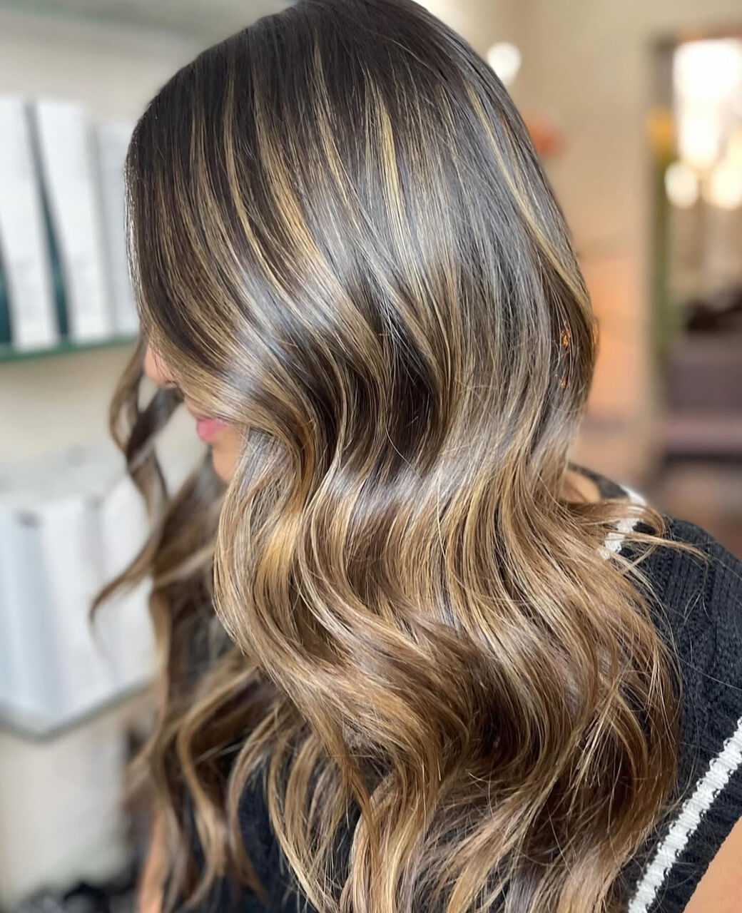 Wavy hair with golden highlights flowing gracefully over a black sweater.